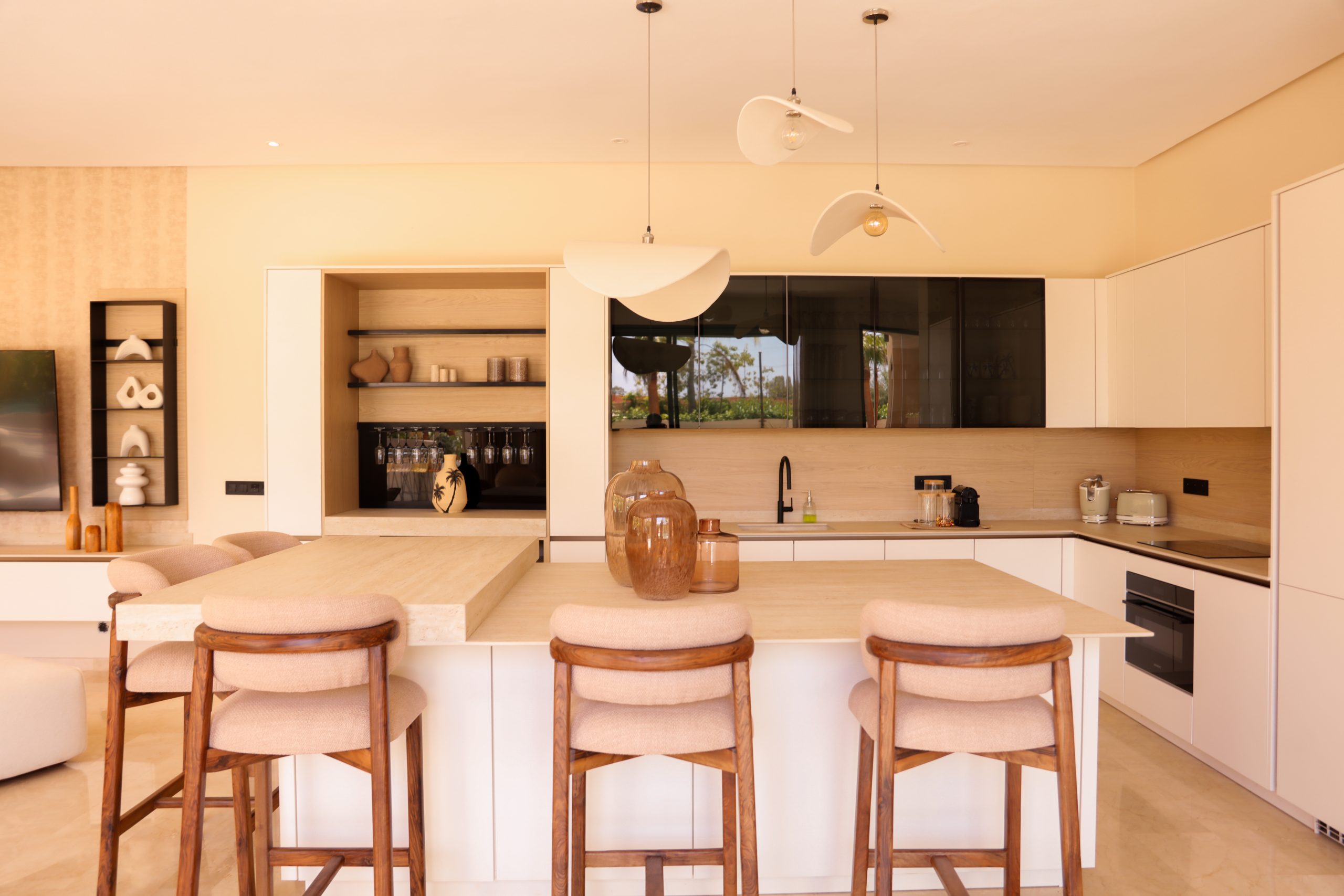 Réalisation client d'une cuisine beige avec îlot central en travertin, vitrines noires fumées et crédence bois, signée KOA Kitchen à Remiremont