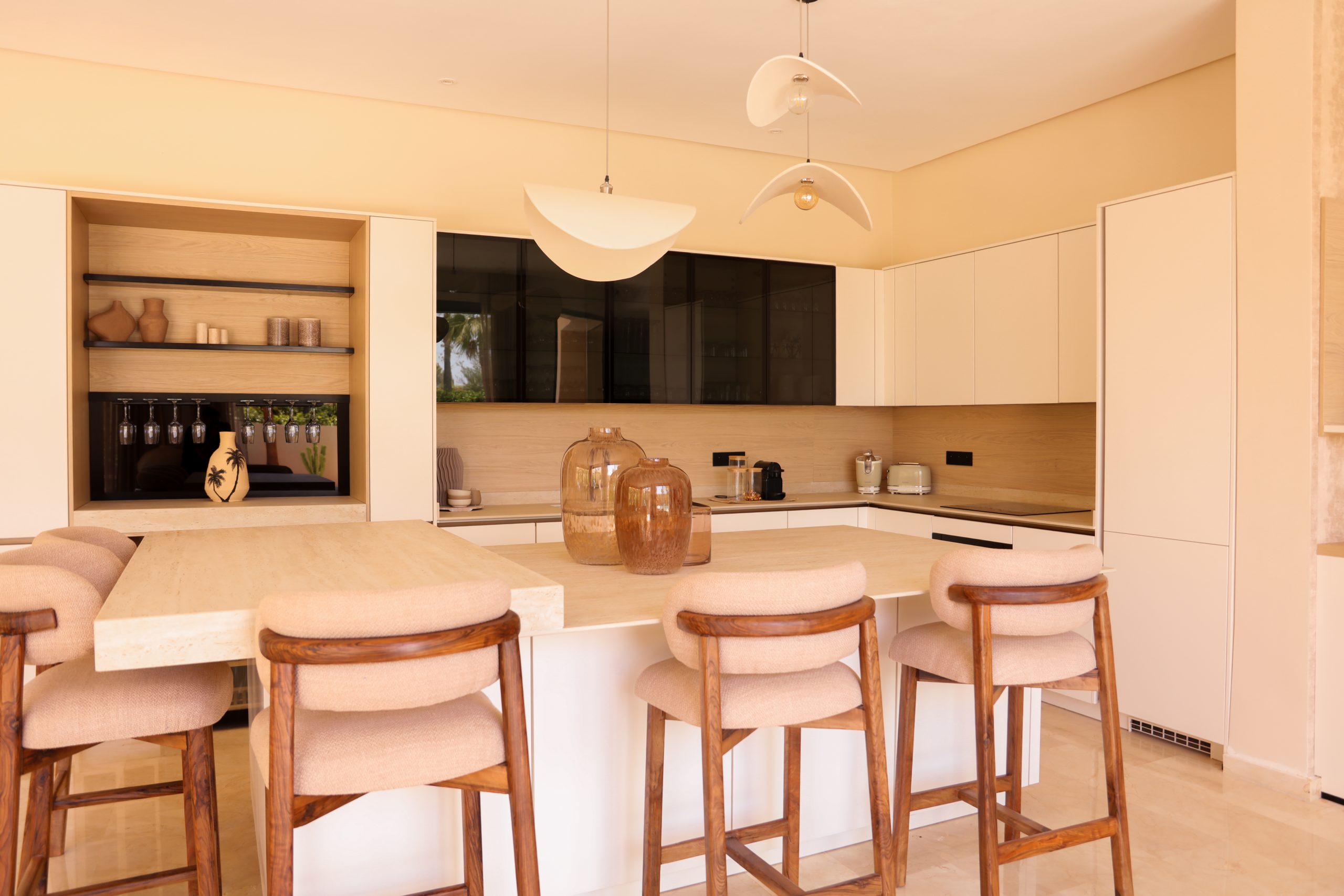 Cuisine sur mesure crème avec îlot central, tabourets en bois massif et suspensions design, installée par KOA Kitchen dans les Vosges