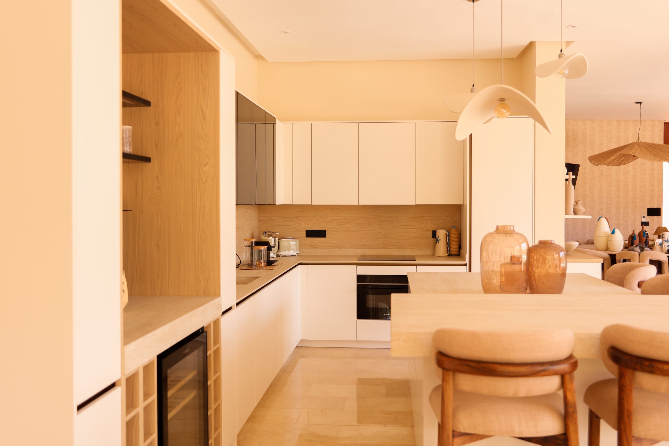 Réalisation d'une cuisine blanche avec cave à vin intégrée, crédence en bois clair et four encastré, conçue par KOA Kitchen à Remiremont