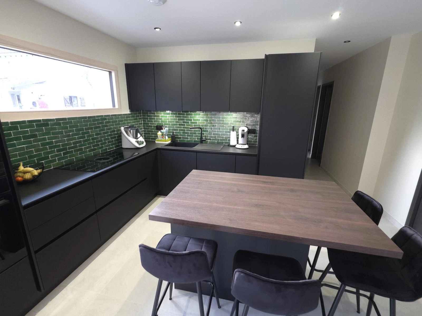 Réalisation client d'une cuisine noire en L avec îlot central en bois et crédence verte, installée par KOA Kitchen à Remiremont