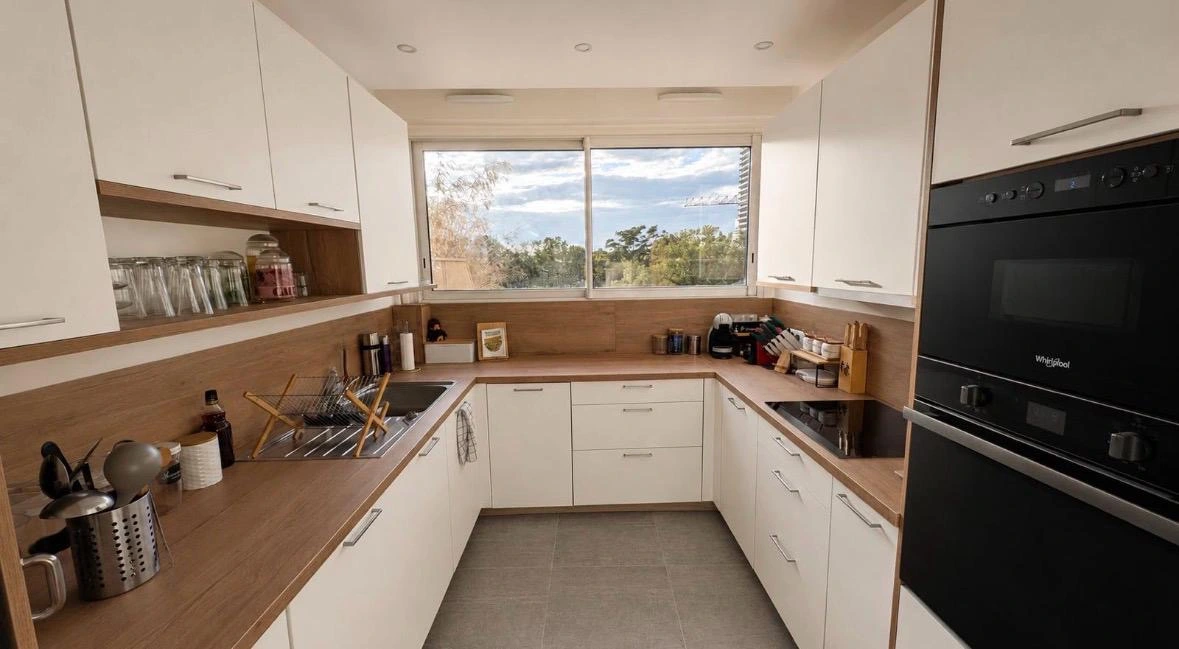 Cuisine en U blanche et bois lumineuse avec fenêtre et fours Whirlpool, réalisation cuisiniste