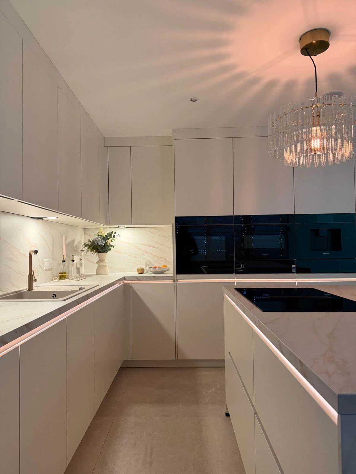 Cuisine sur mesure blanche avec îlot marbré, lustre en verre et éclairage LED, réalisée par KOA Kitchen, cuisiniste Vosges